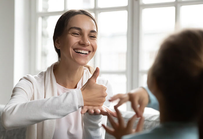 smiling woman uses sign language with a child
