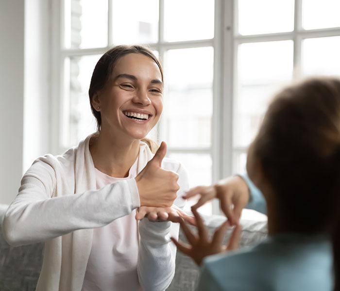 smiling woman uses sign language with a child