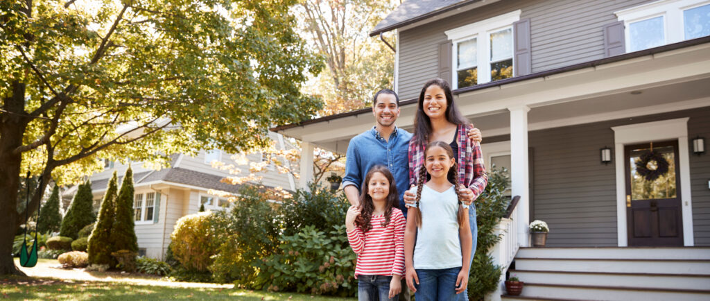 Smiling Family Standing In Front Of Their Home