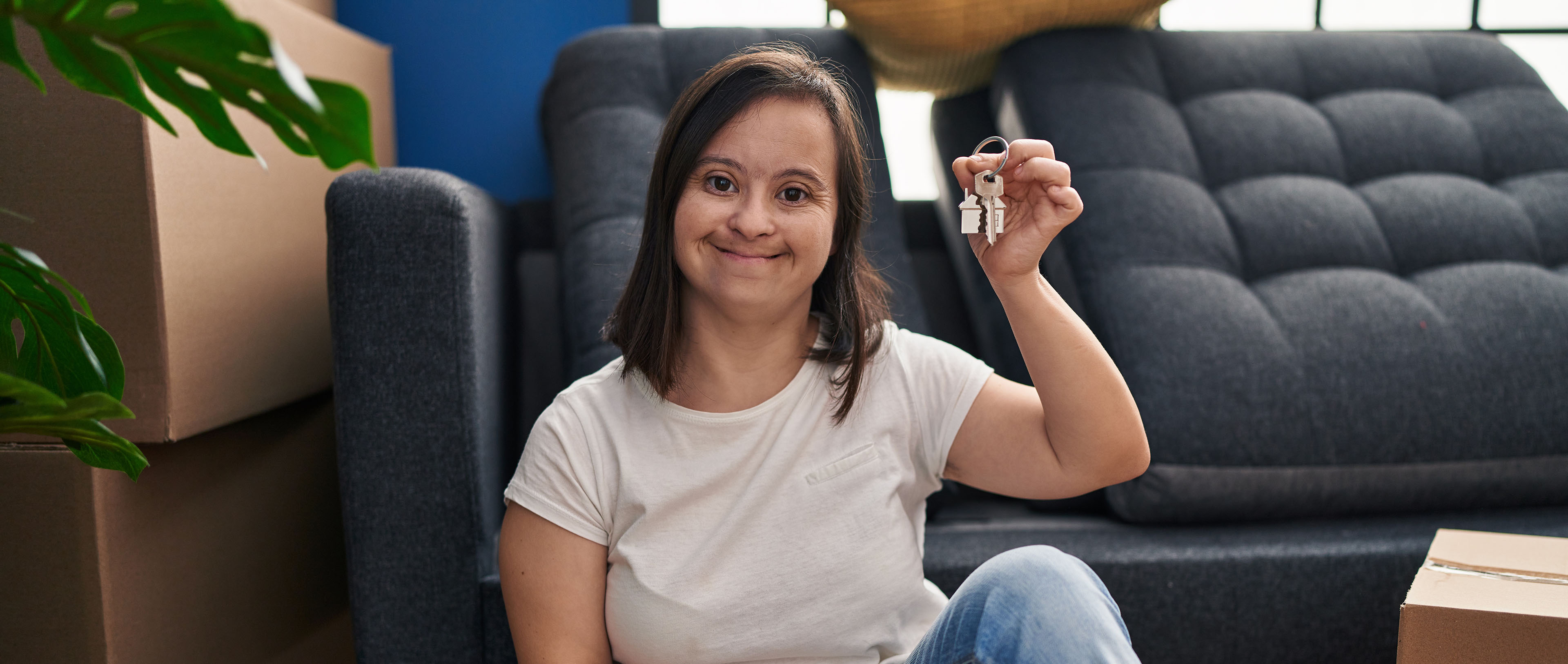 Down syndrome woman smiling confident holding key sitting on floor at new home